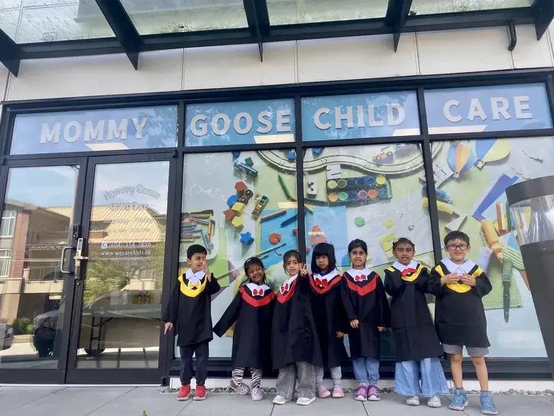 Graduating children in caps and gowns outside the Mommy Goose Child Care Sullivan entrance.