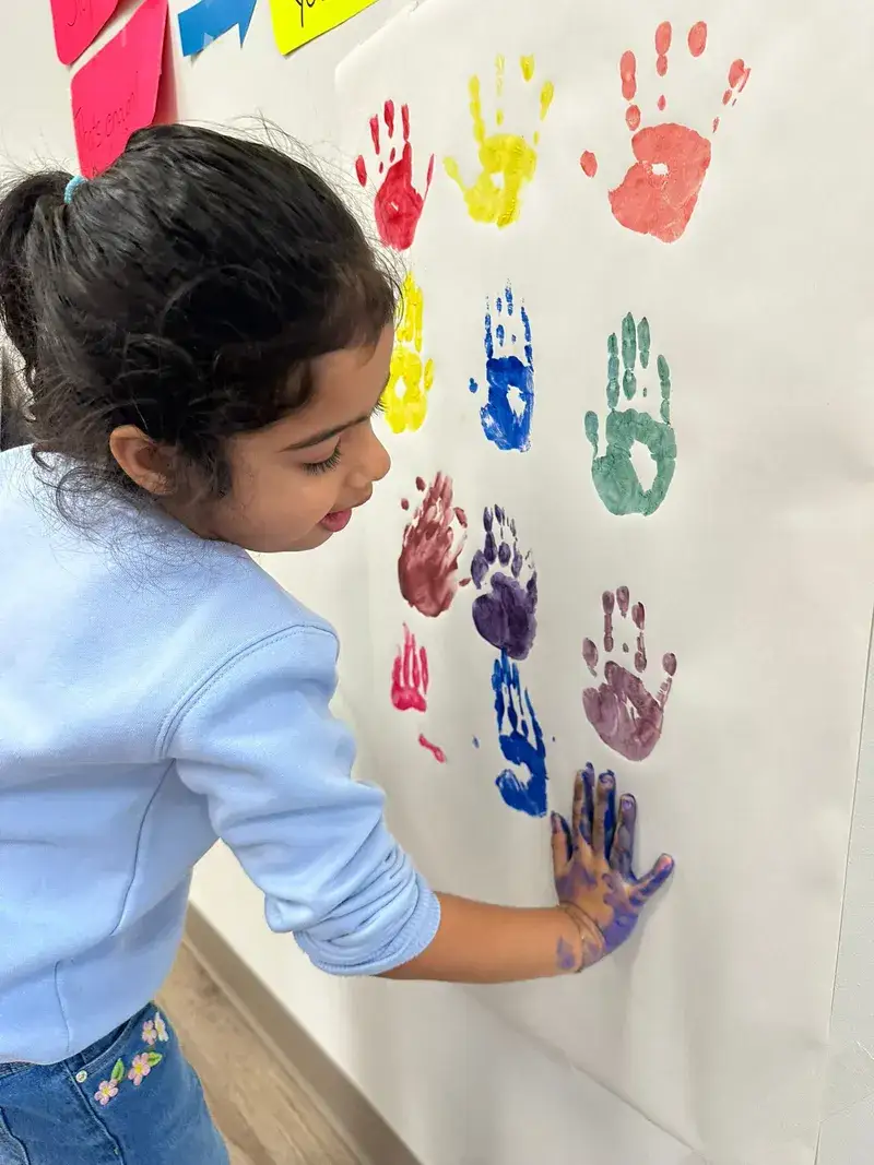 Child pressing colourful painted handprints onto paper.