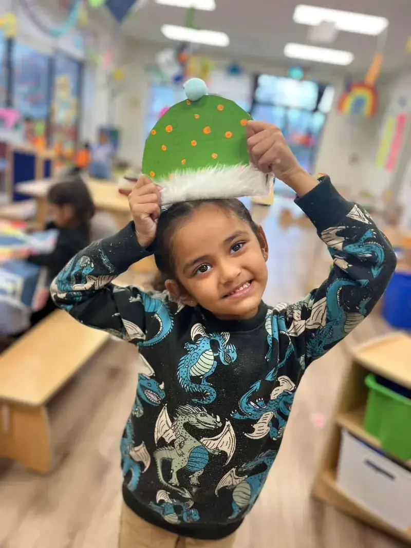 Smiling child holding a handmade paper hat above their head.