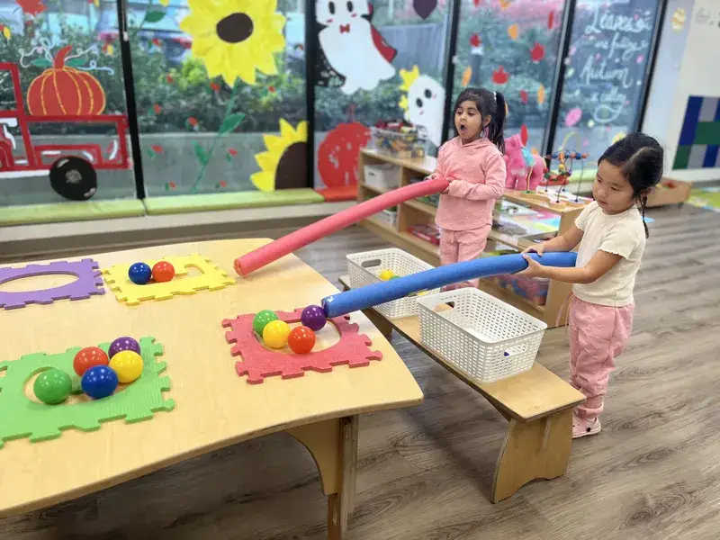 Children guiding balls through foam tubes at a play table.