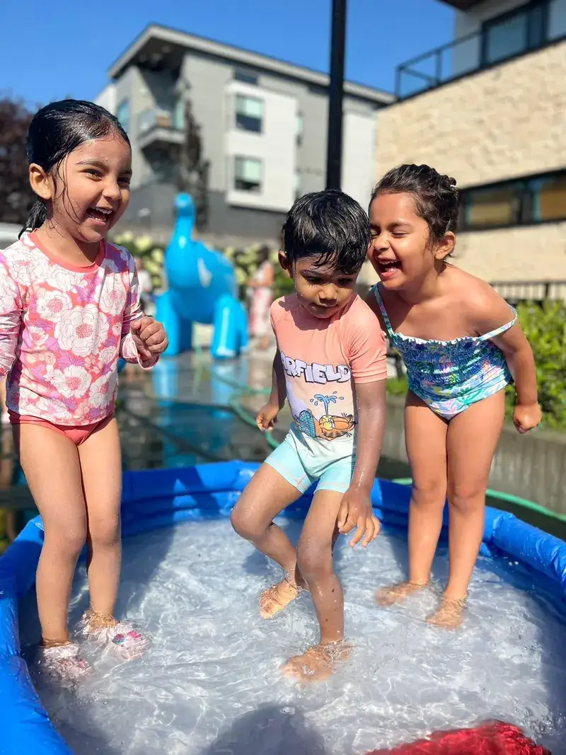 Children splashing and laughing in a paddling pool on a sunny day.
