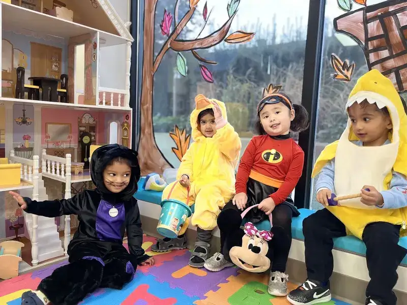Children dressed in costumes sitting together by the classroom window.