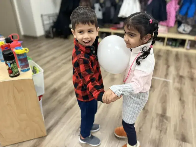 Two children dancing together while holding a balloon.