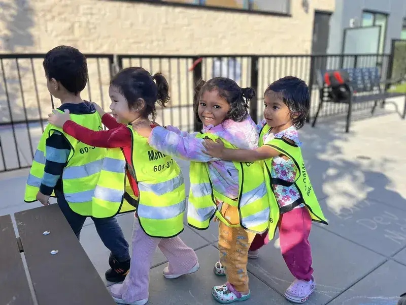 Children in safety vests walking together in a line outdoors.